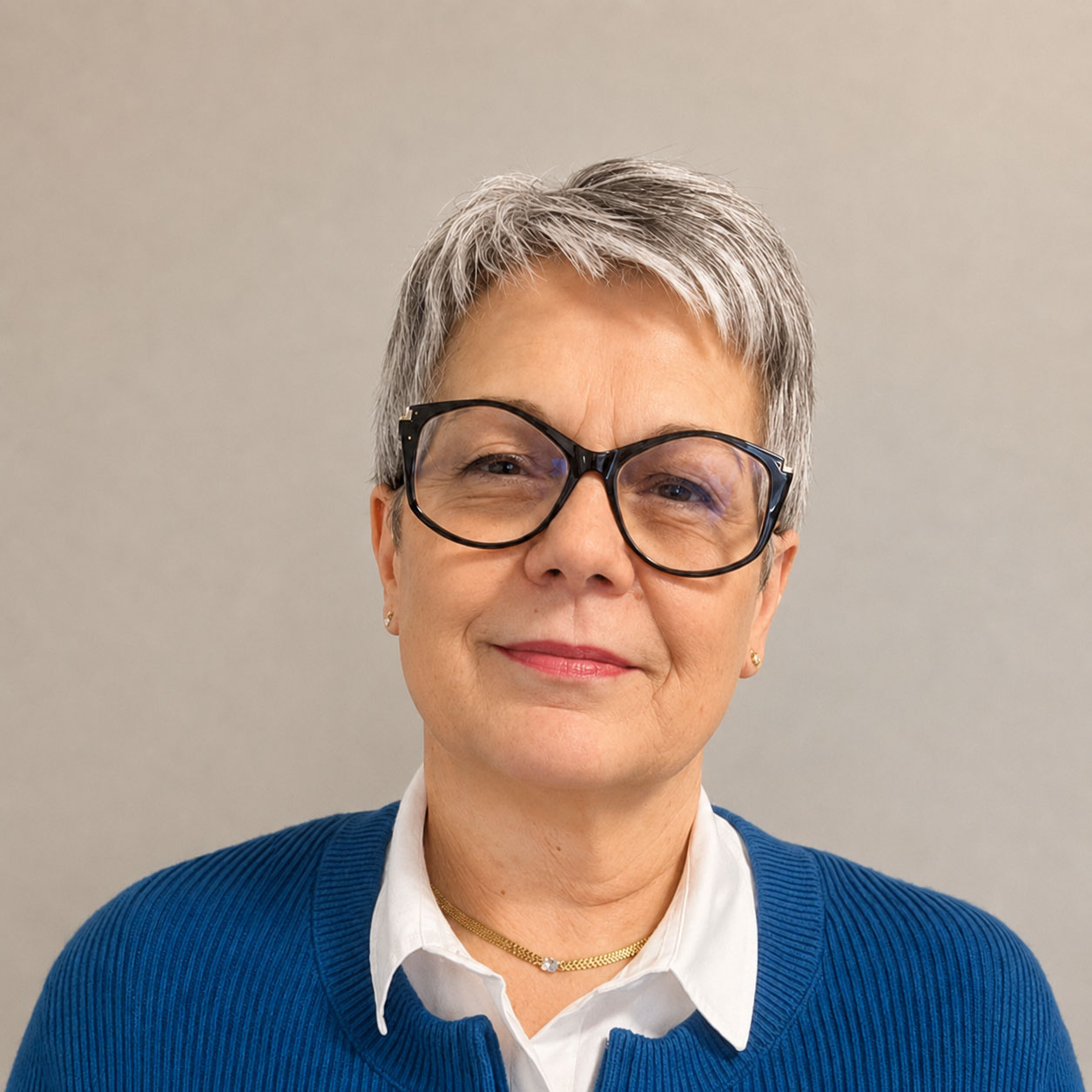 Eine Frau mit kurzen grauen Haaren, einer großen schwarzen Brille und einem blauen Pullover über einem weißen Hemd mit Kragen blickt vor einem schlichten Hintergrund in einem Seniorenheim in Lohne in die Kamera.